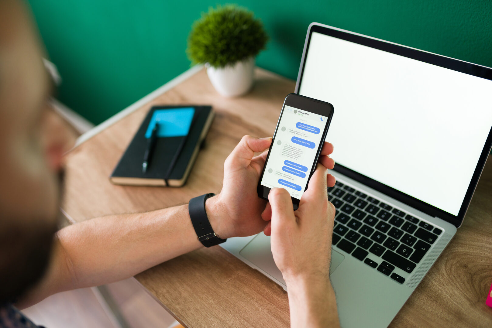 Man texting on phone with chat app near laptop