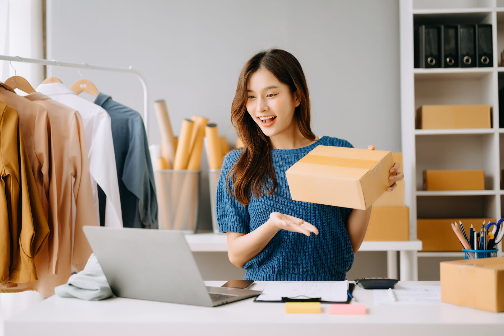 Woman with laptop packing order while checking phone